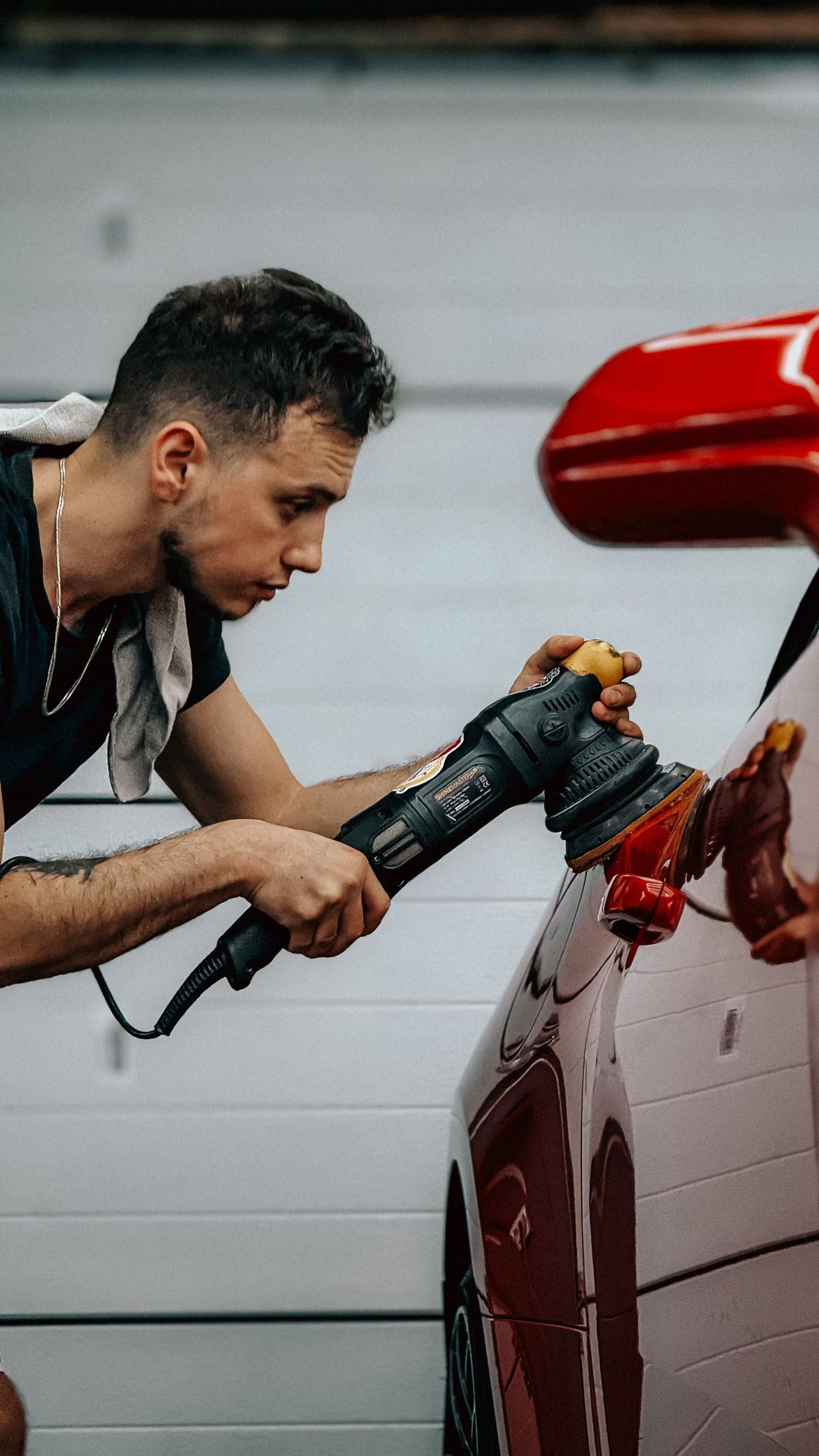 Detailer polijst het paneel van een rode wagen met een machine
